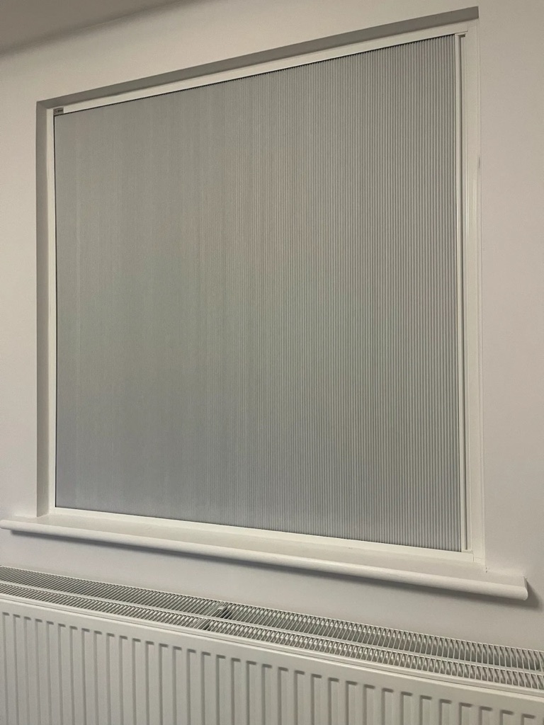 Blind Screen pulled down across a bedroom window in its white side channels, blocking out the daylight