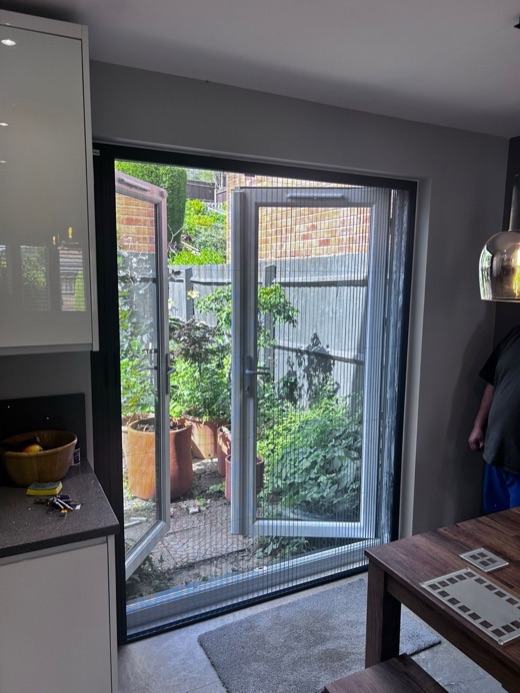 French doors open with the BlindScreen bug-screen mesh pulled across the opening, garden visible behind
