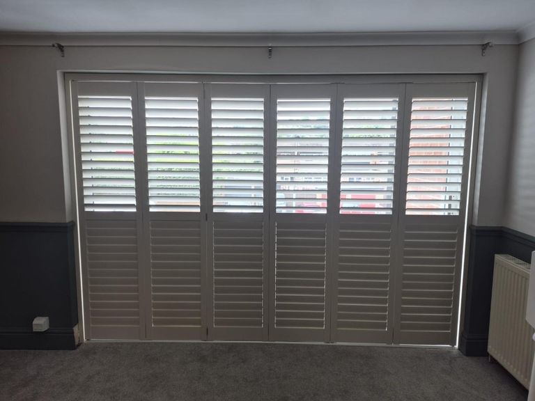 Bridgnorth living room with six-panel tracked shutters in Ivory Lace, lower louvres closed and upper louvres tilted open