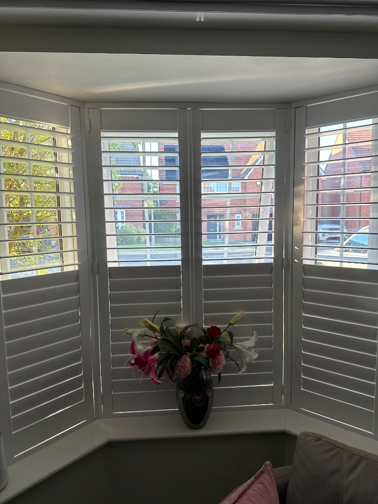 White plantation shutters fitted in a three-panel bay window, top louvres open and bottom louvres closed for privacy