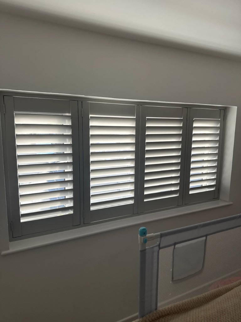 White plantation shutters fitted across a wide window with louvres tilted open for daylight