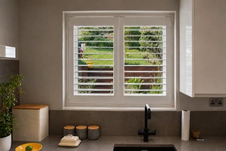 Stourbridge kitchen with full height white plantation shutters above the sink, louvres tilted open showing the garden beyond
