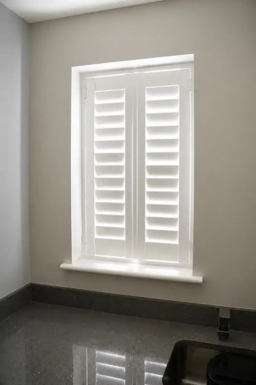 Utility room in Stourbridge with a full height white plantation shutter, top louvres tilted open and bottom louvres closed showing the split-tilt feature