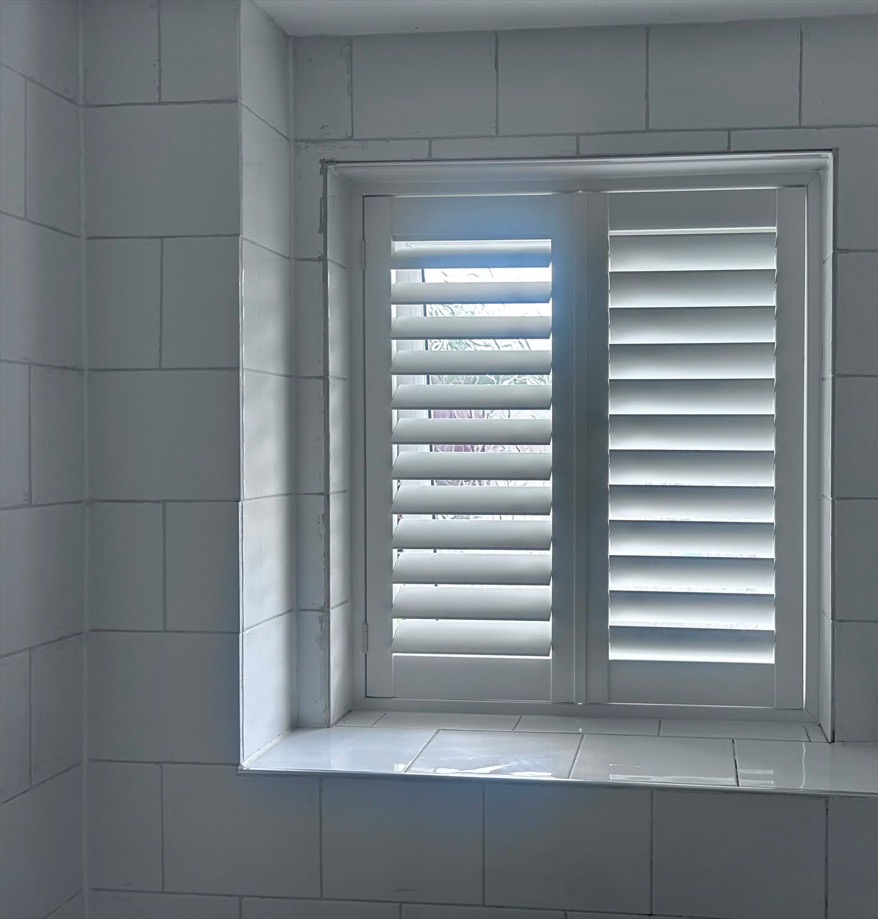 Wednesbury bathroom composite shutters in Silk White with one panel open and one closed inside white wall tiles