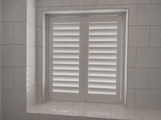 Wednesbury bathroom with two-panel full height composite shutters in Silk White fitted inside a white tiled reveal, louvres closed