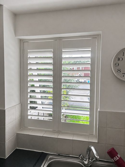 Wednesbury kitchen with full height composite shutters in Silk White over the sink, louvres tilted open showing the garden