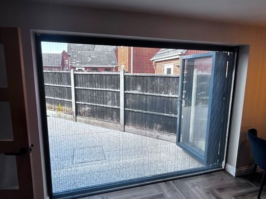 Grey-framed BlindScreen insect mesh pulled across bi-fold patio doors with the doors folded back
