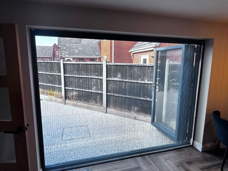 Grey-framed BlindScreen insect mesh pulled across bi-fold patio doors with the doors folded back