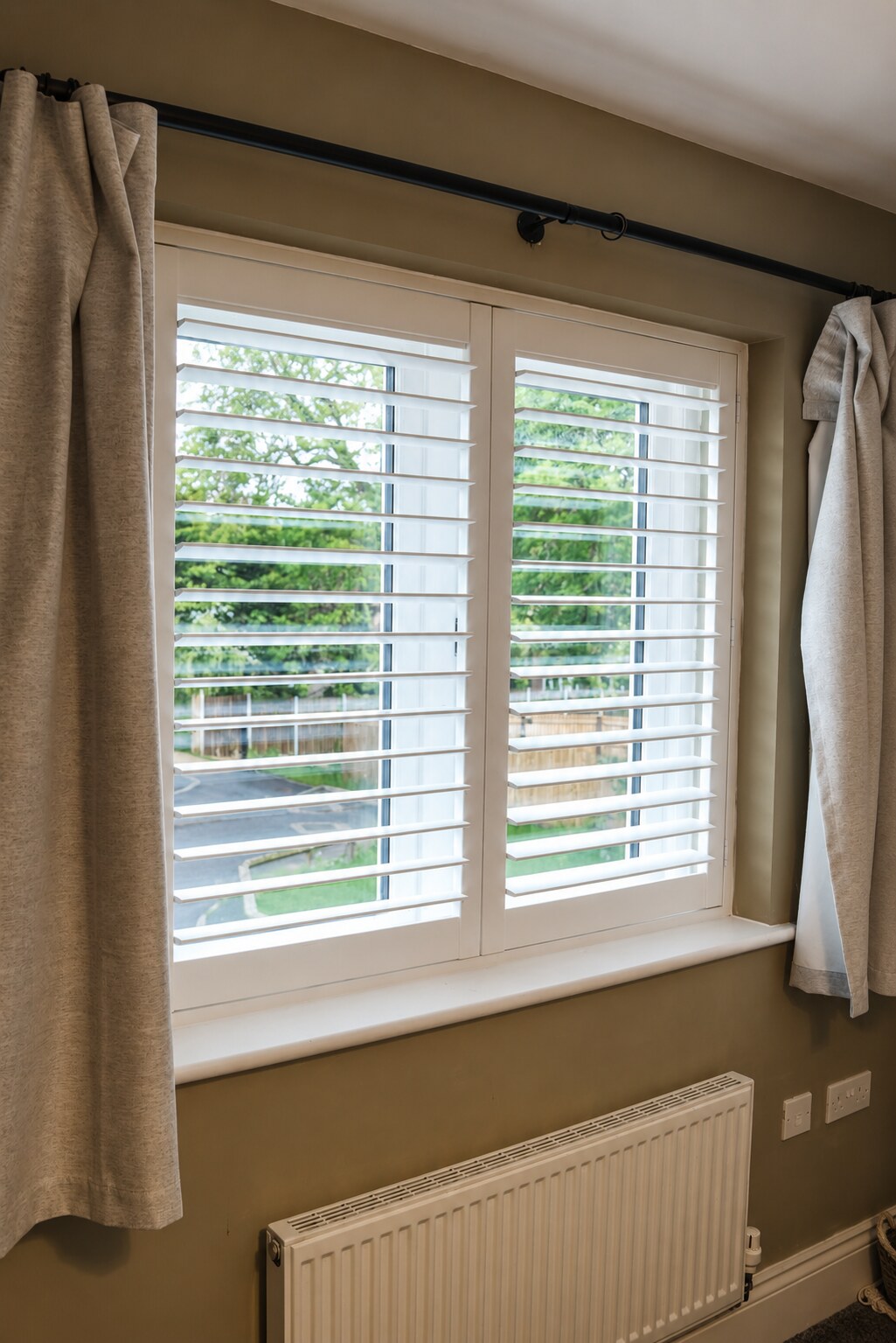 Albrighton bedroom with Silk White composite shutters, louvres tilted open showing the garden beyond