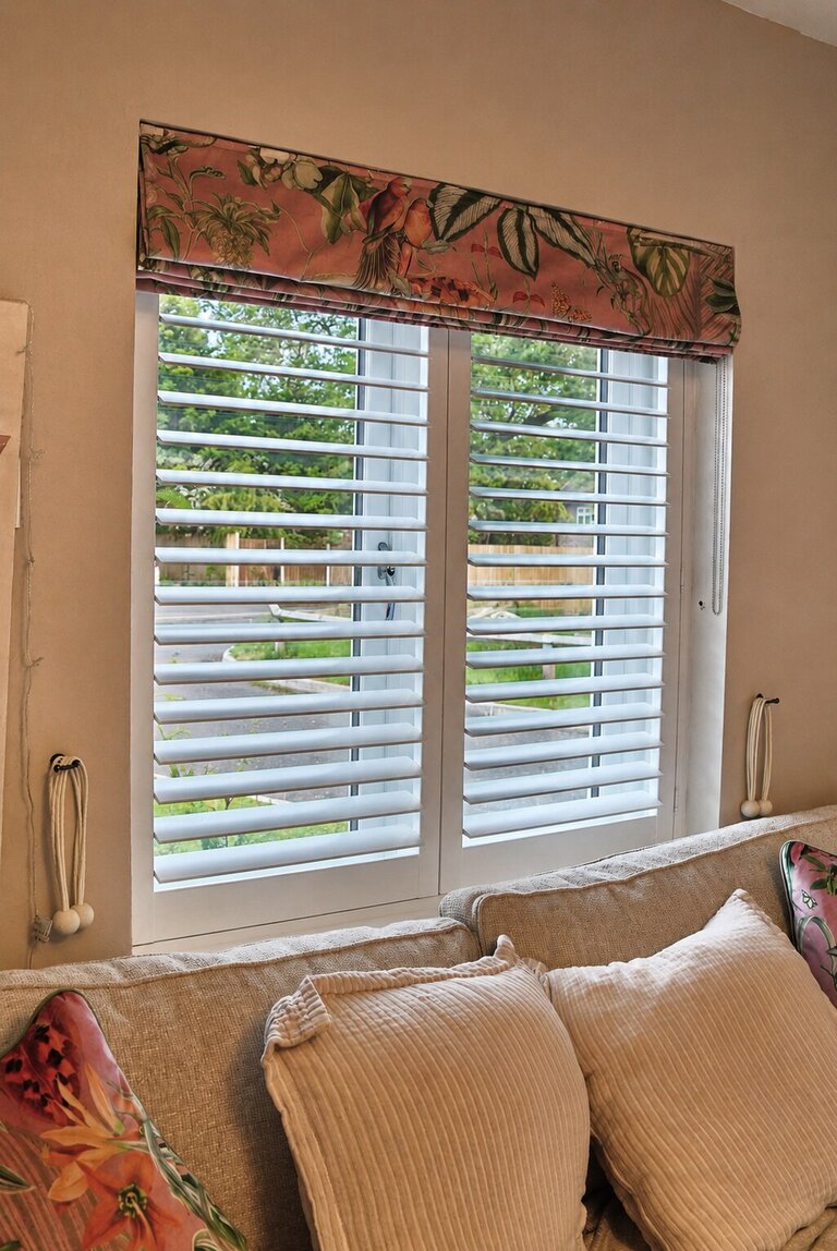 Albrighton living room with Silk White composite shutters, louvres tilted open below a tropical-print Roman blind
