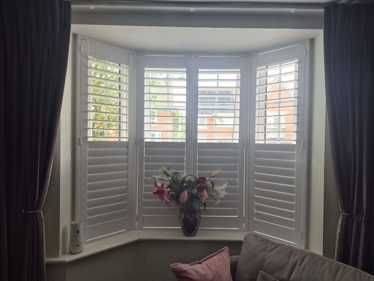 Baggeridge living room bay with four-panel Pure White engineered wood shutters, split tilt with upper louvres open and lower louvres closed