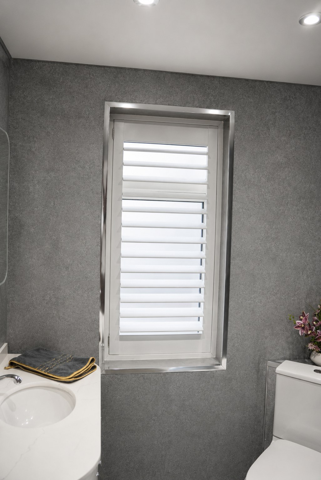 Brierley Hill bathroom waterproof shutters in Pure White with louvres tilted open, vanity and toilet visible below the window