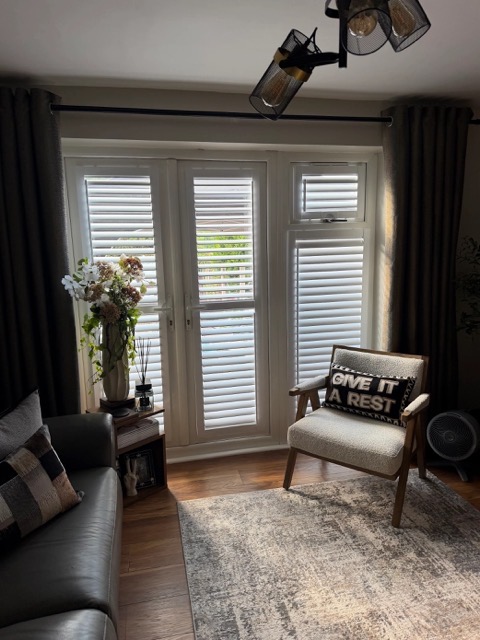 White full height shutters on French doors and a side window, louvres tilted open in a living room