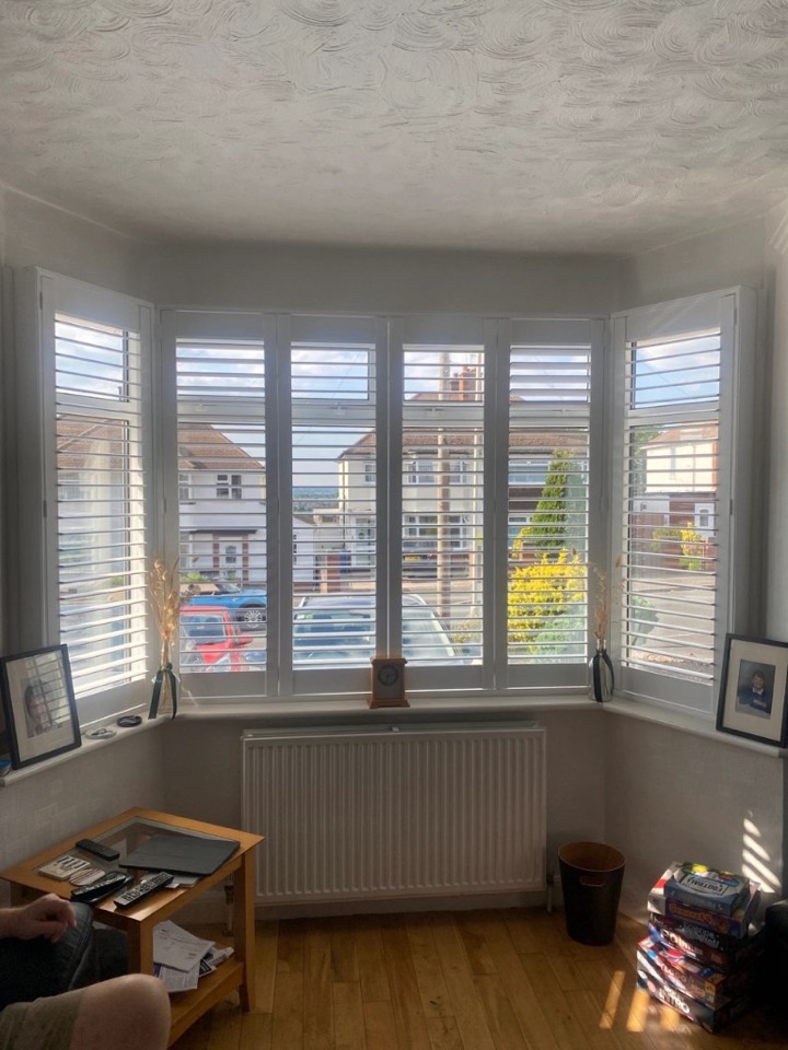 White full height shutters with mid-rail on a four-panel bay window, louvres partially open