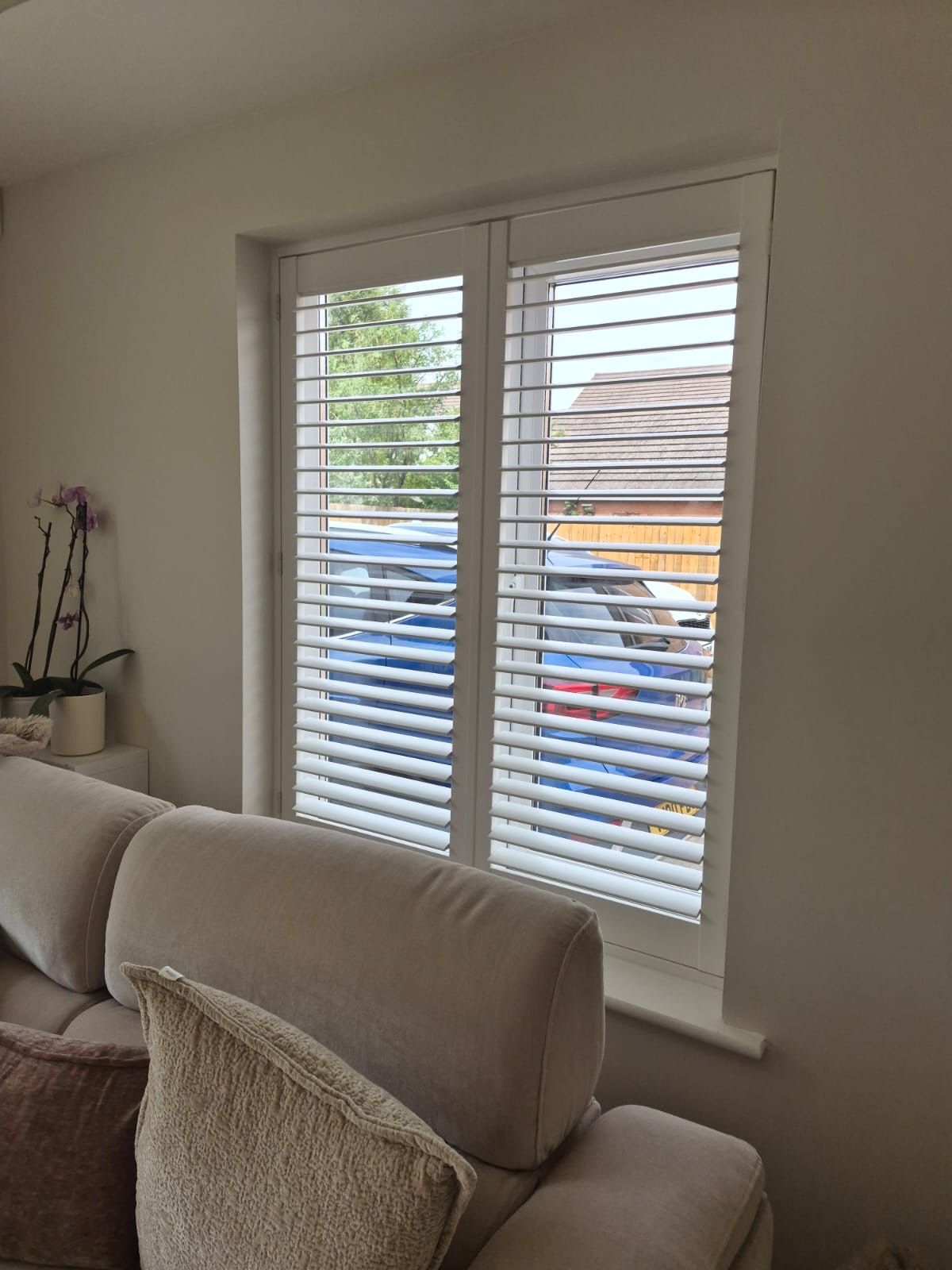 Kingswinford living room composite shutters in Silk White above the sofa, louvres tilted open