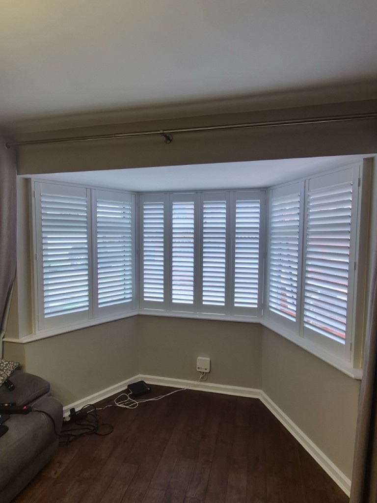Netherton living room bay Pure White composite shutters across the full bay, louvres partially closed