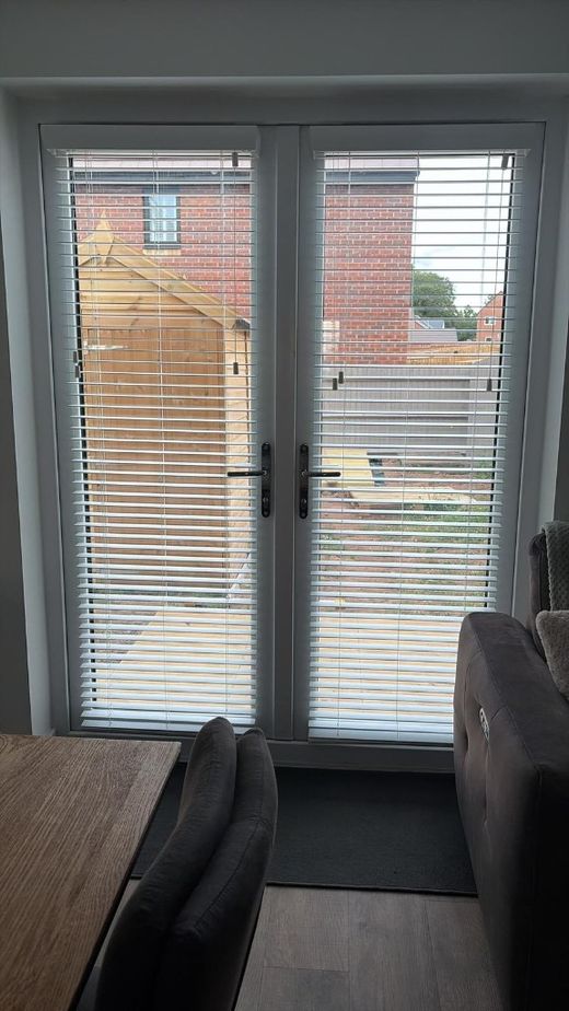 Stafford French patio doors with white faux wood venetian blinds face-fixed to each door, slats open with the garden visible behind