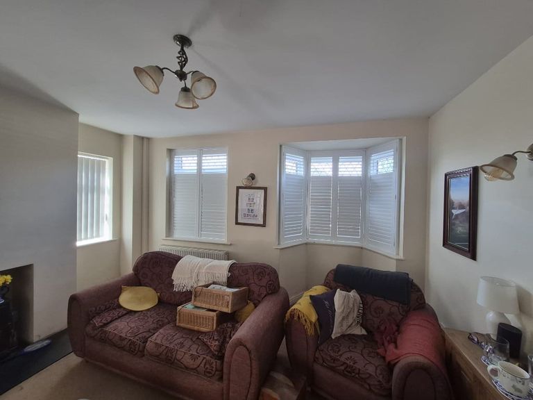 Living room with Pure White full height composite shutters on a flat window and four-panel bay, upper louvres open and lower louvres closed