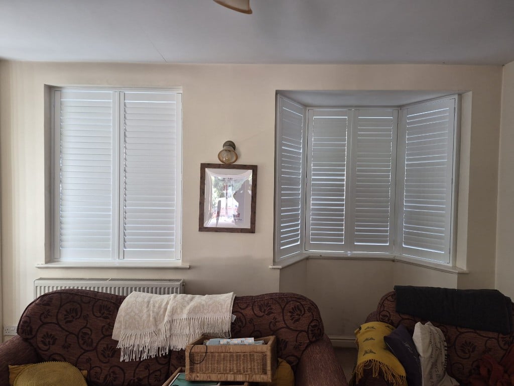 Living room Pure White composite shutters with louvres partially open across flat and bay windows