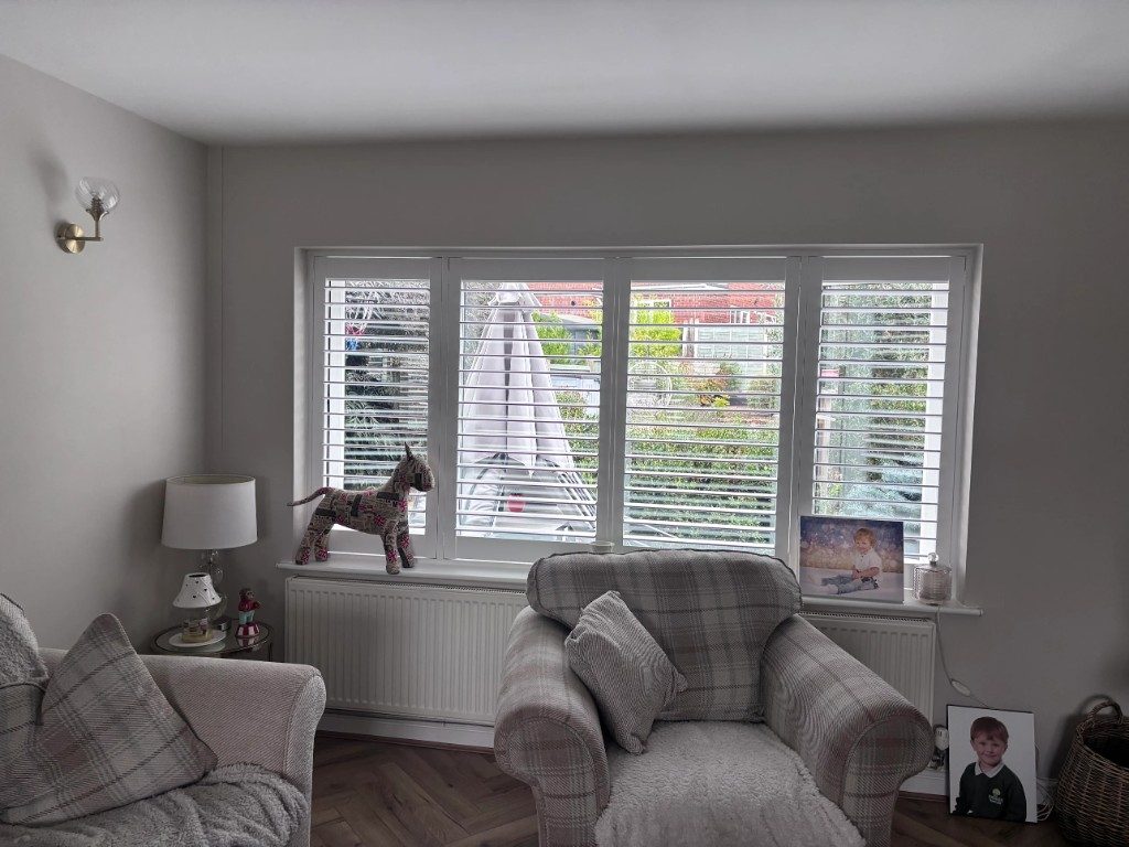 Pure White full height shutters on a four-panel living room window facing the garden, louvres open