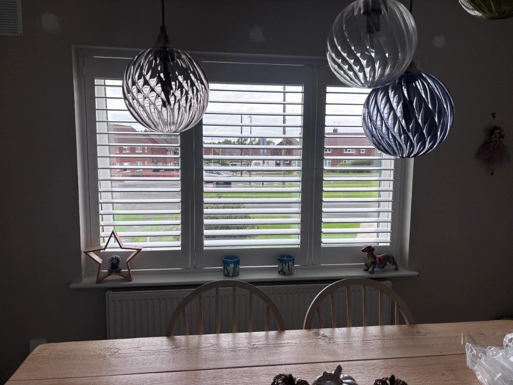 Pure White full height shutters on a three-panel dining area window facing the street, louvres open