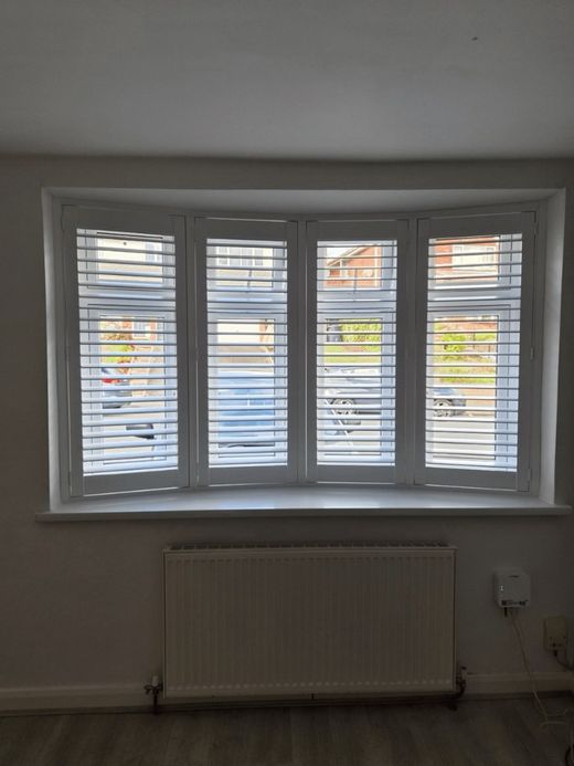 Full height White shutters across a four-panel front-facing bay window in Halesowen, louvres open towards the street