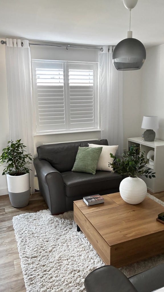 Pure White full height shutters with 76mm louvres on a window with sheer curtains in a modern living room