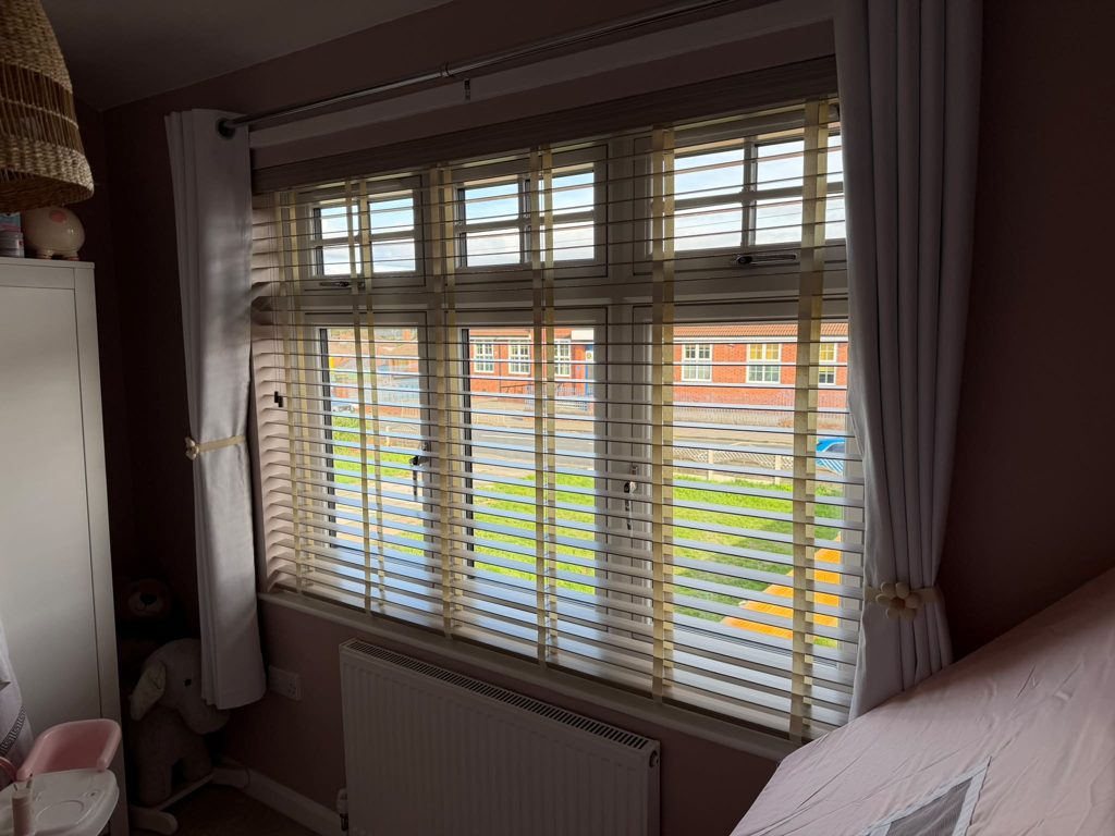 Front bedroom window in Bilston with a 50mm Greige faux wood venetian blind beside a curtain, slats open to the street