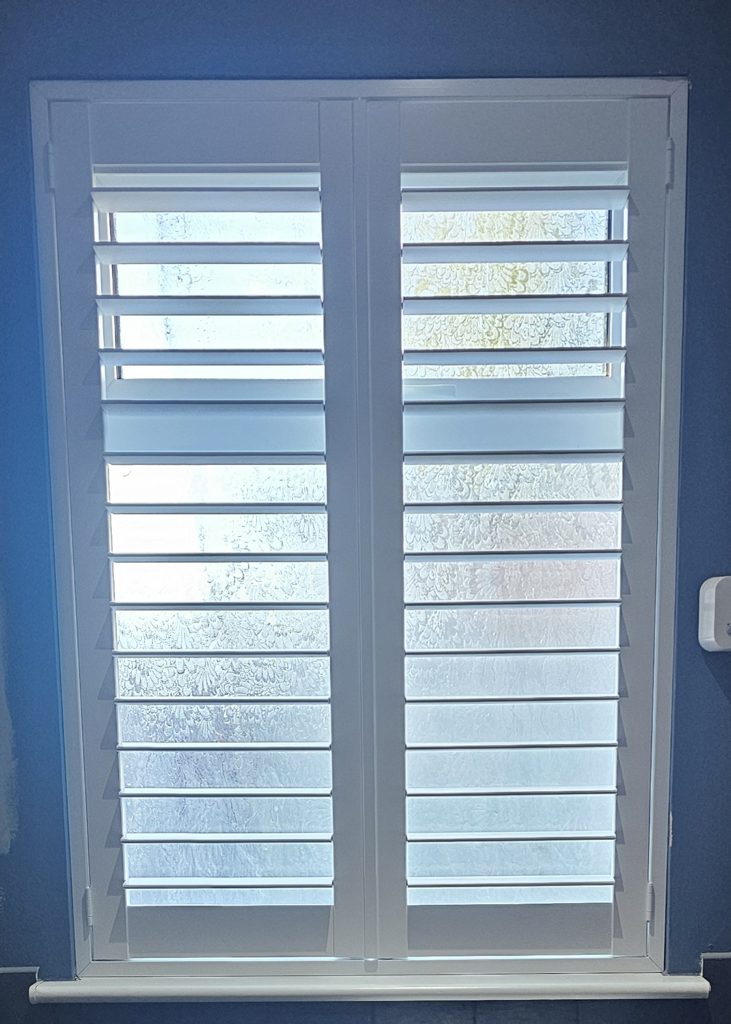 Two-panel Pure White ABS plastic shutter on the small Bilston kitchen window with the louvres open and daylight coming through the patterned glass