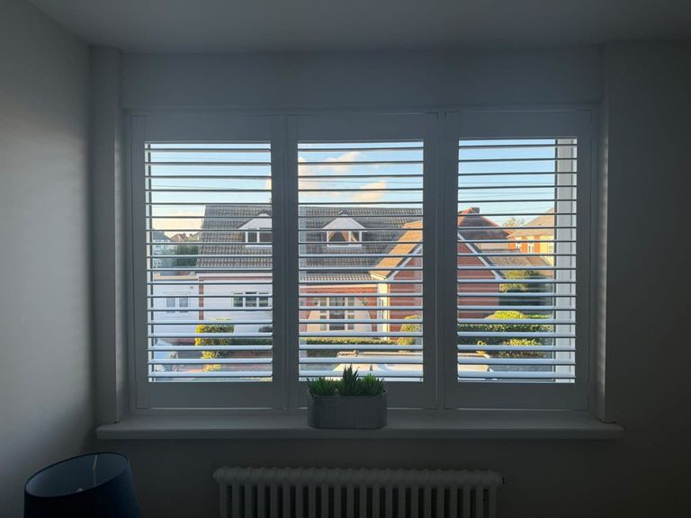 Three-panel full height Pure White shutters with 63mm louvres in a Halesowen bedroom, louvres open to the street