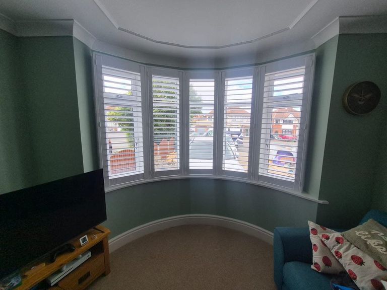 Full height Pure White engineered wood shutters with 76mm louvres across a five-section curved bay window in a Halesowen living room