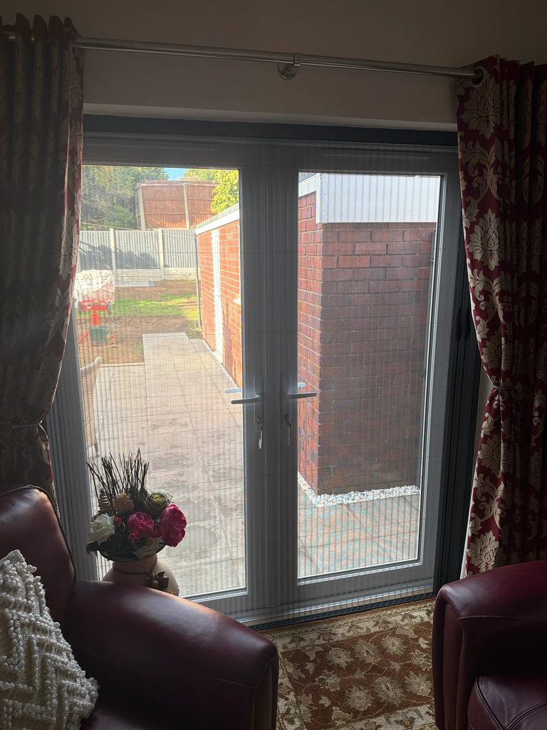 Grey-framed BlindScreen with the grey bug screen pulled across French doors to the garden in a Kinver spare room