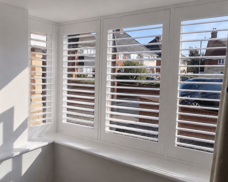 White plantation shutters fitted to a Birmingham bay window, following the angles of the bay across the front of a living room