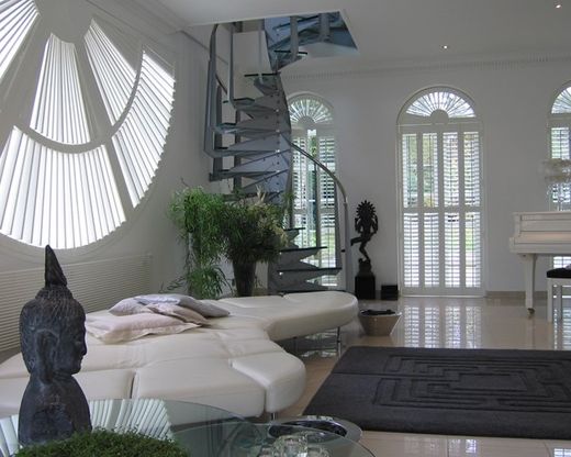 Open-plan West Midlands home with three different special shapes by Greystone Shutters: a fan-pattern circular shutter on a porthole window, plus tall arched-top shutters across the rear elevation, louvres set to filter daylight