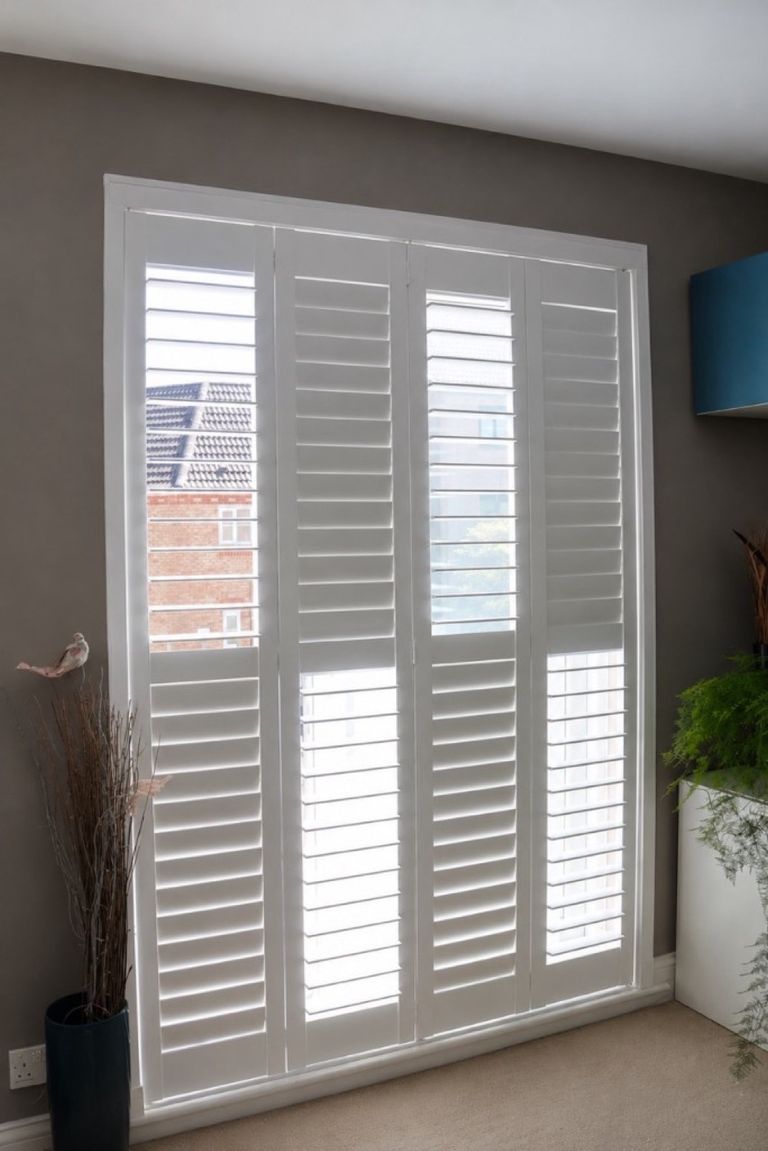 Four white tracked shutter panels fitted across a tall living room window in Tipton, louvres closed for privacy